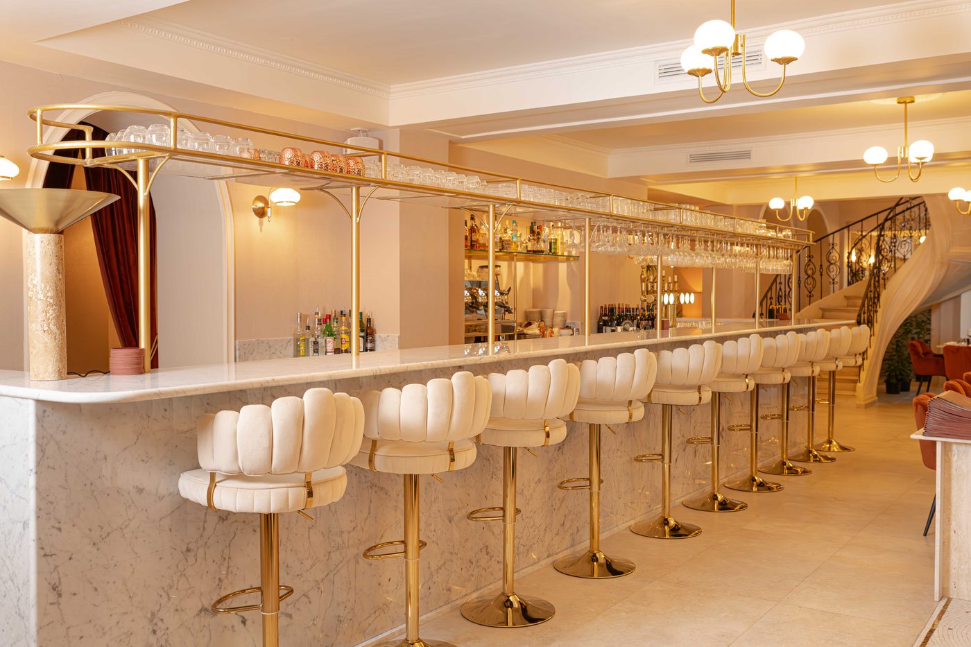 Le long bar en marbre blanc de Magdalena, tabourets blancs à pieds dorés, escalier au fond