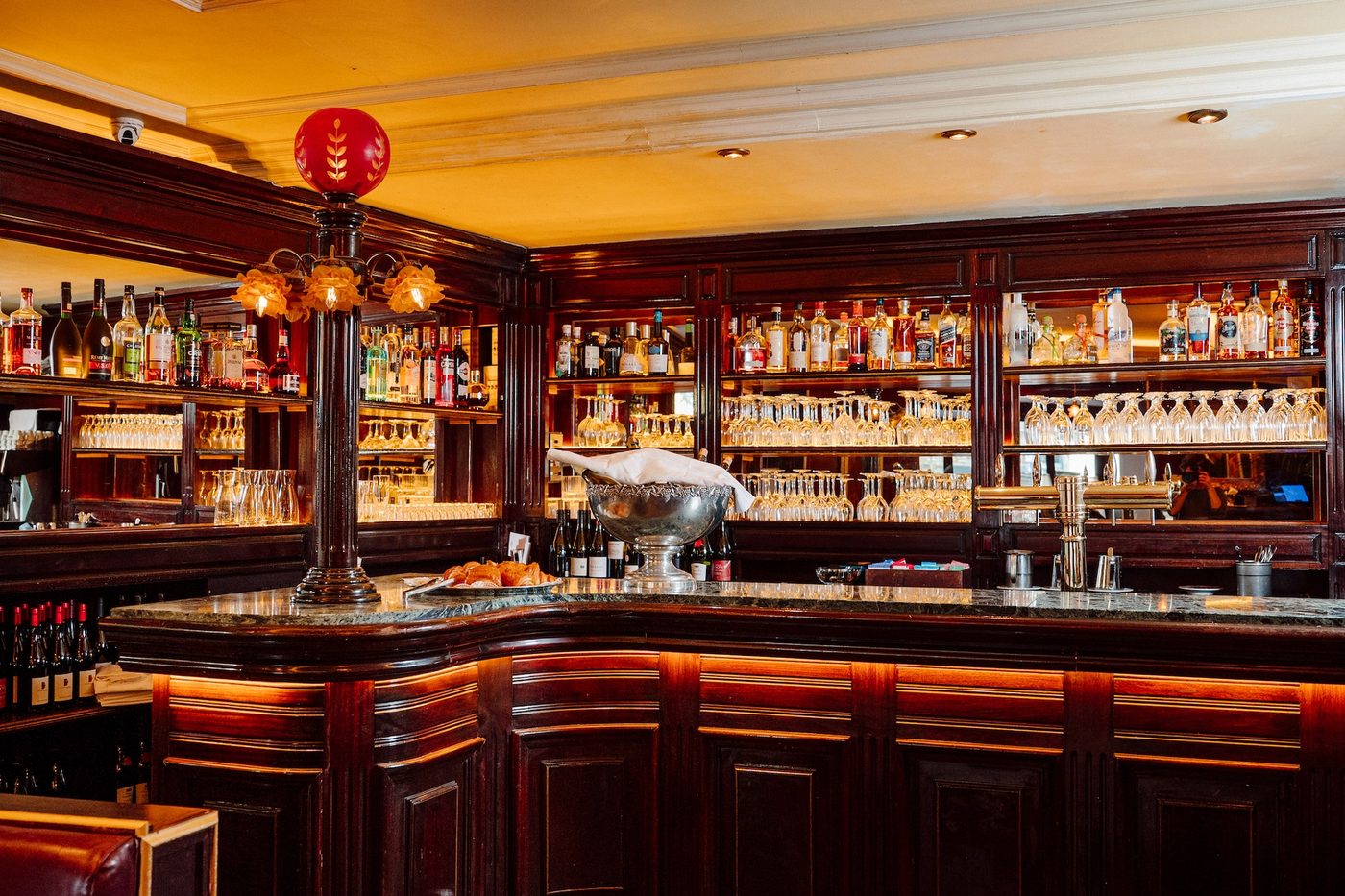 Le bar du Maresquier, comptoir d'acajou à plateau de marbre vert, lampadaire à globe rouge et étagères de bouteilles