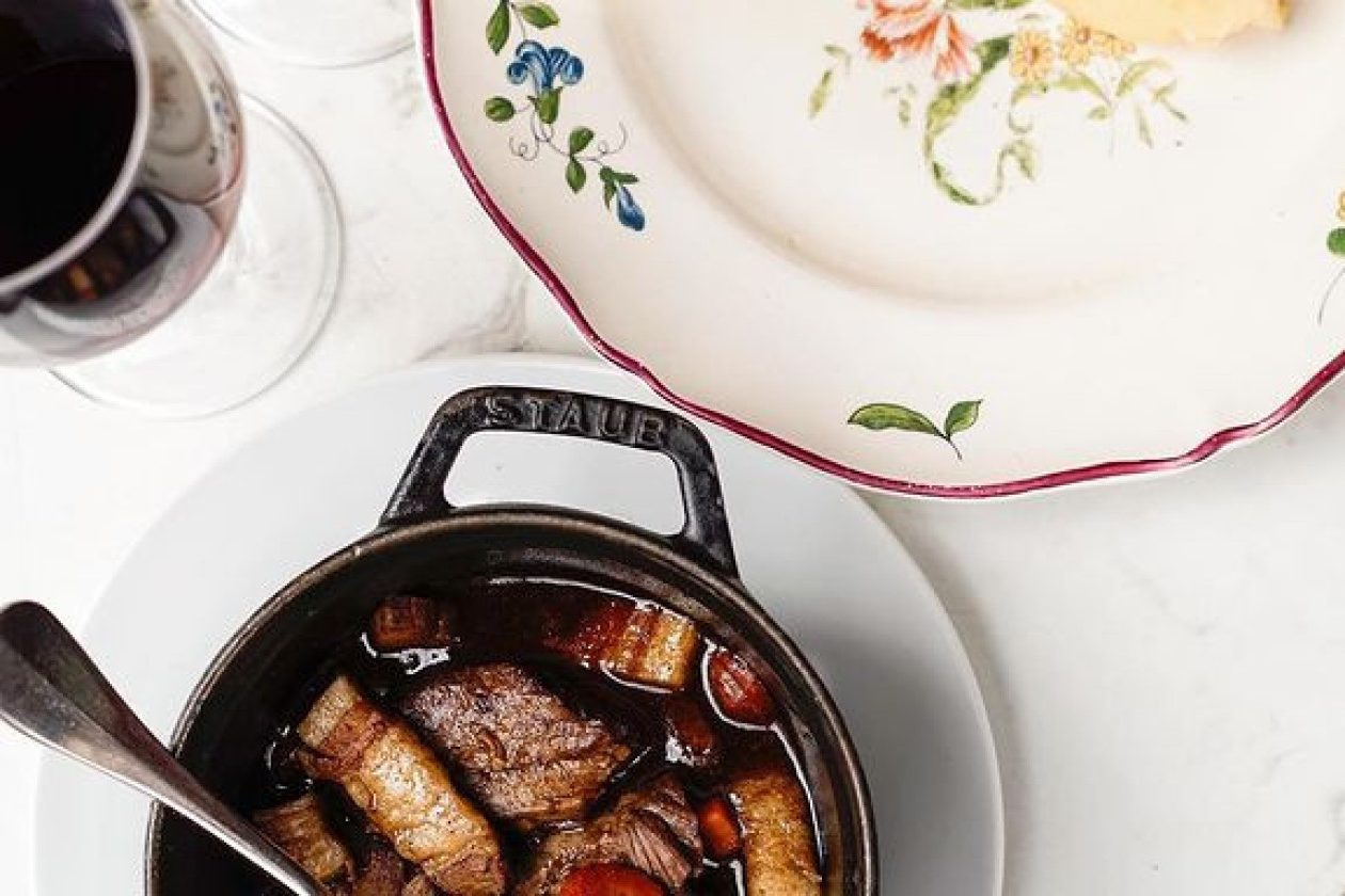 Un bœuf bourguignon en cocotte, une assiette ancienne à motifs floraux et un verre de vin rouge