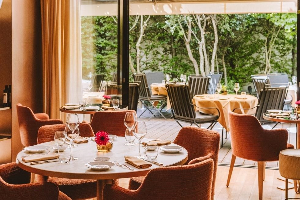 La salle d'Il Ristorante Niko Romito, tables rondes et fauteuils orangés, ouverte sur le jardin du Bulgari Hotel Paris