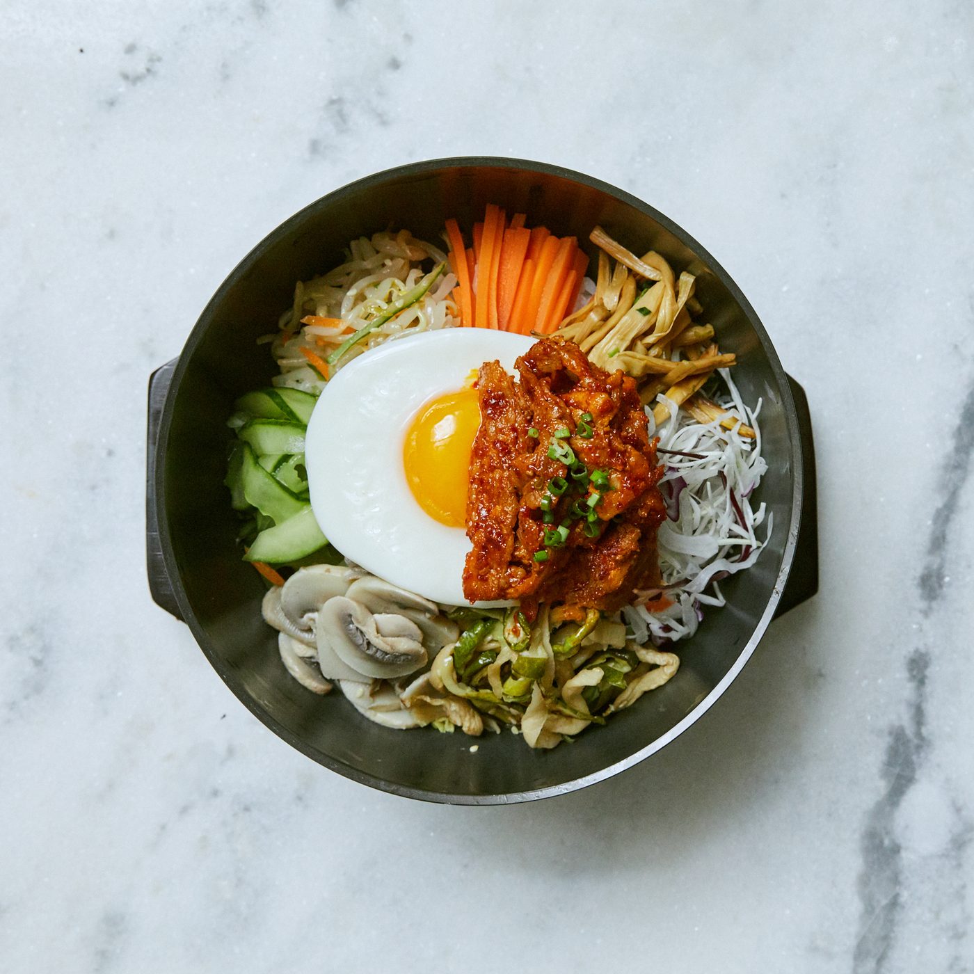 Un bibimbap dans un bol noir, œuf au plat, légumes en julienne et viande épicée, chez On the Bab