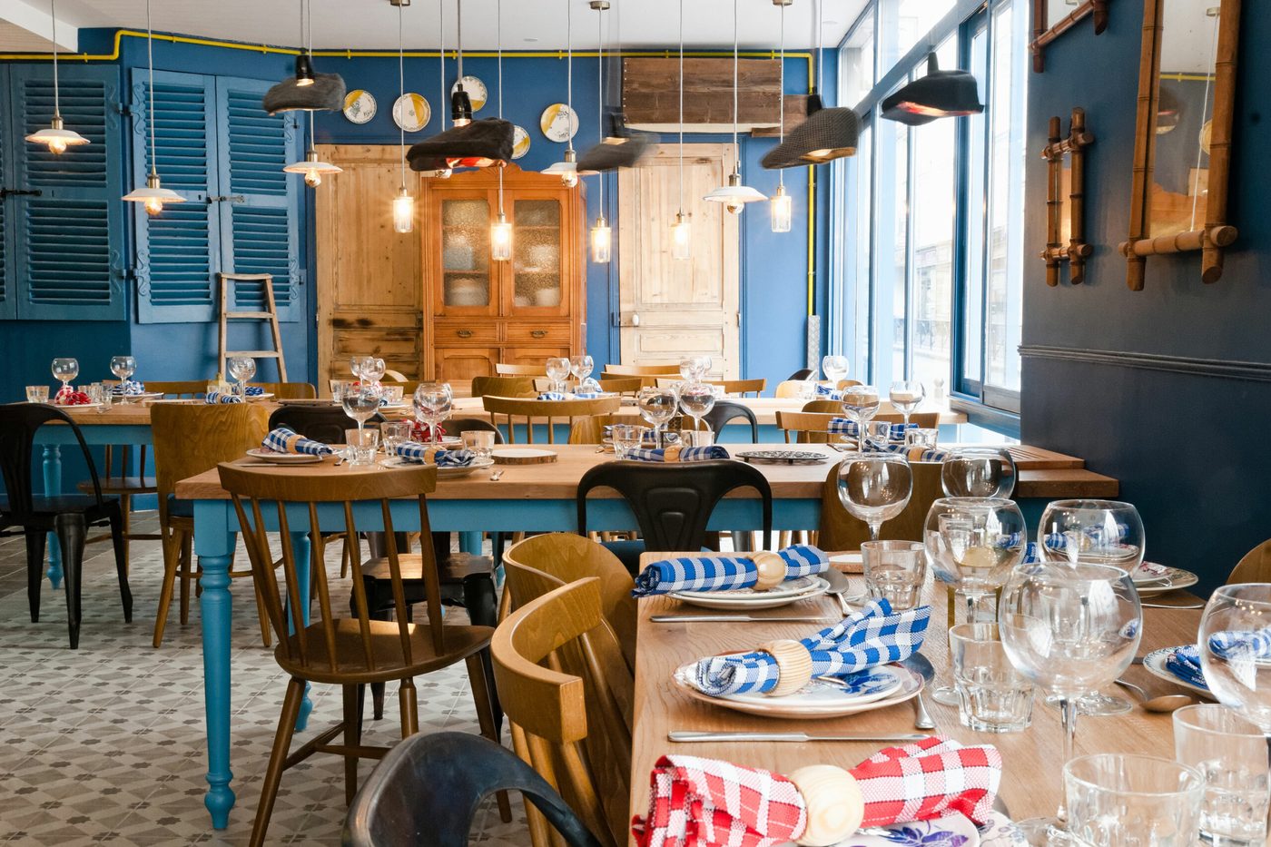 La salle de Papy aux Fourneaux, longues tables de bois aux pieds bleus, serviettes à carreaux et chaises dépareillées