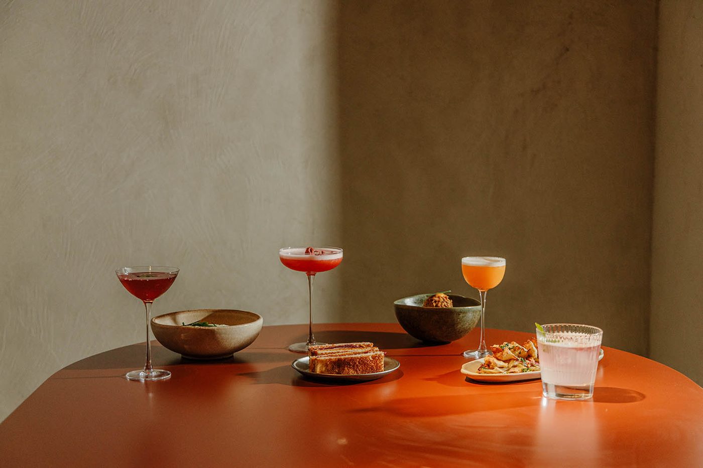 Trois cocktails et des assiettes à partager sur une table orange chez Persimmon's