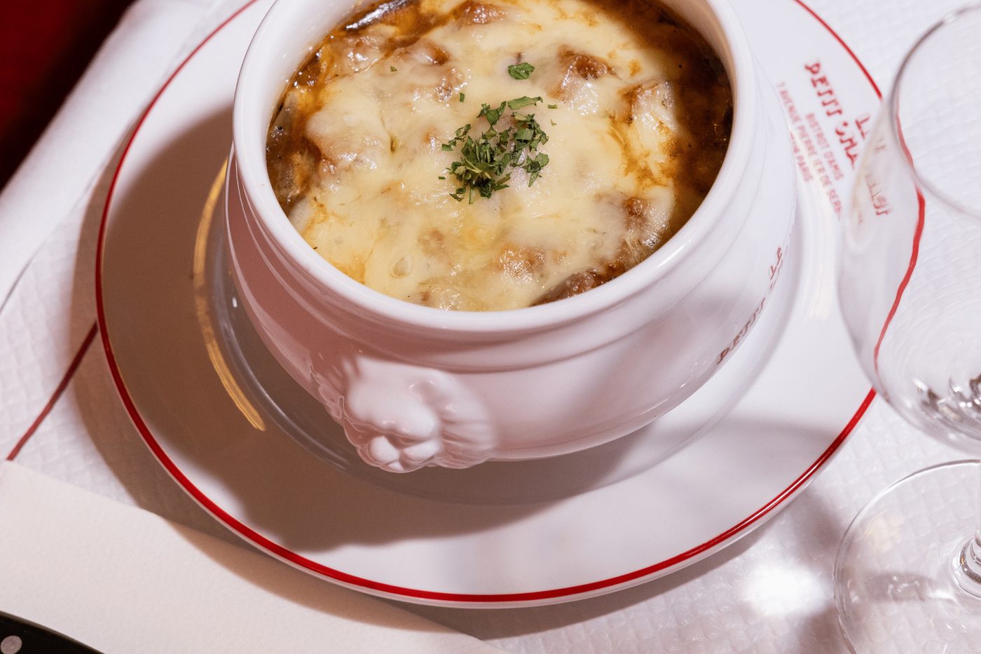 Une soupe à l'oignon gratinée dans une soupière blanche, sur une assiette au nom du Petit Chaillot