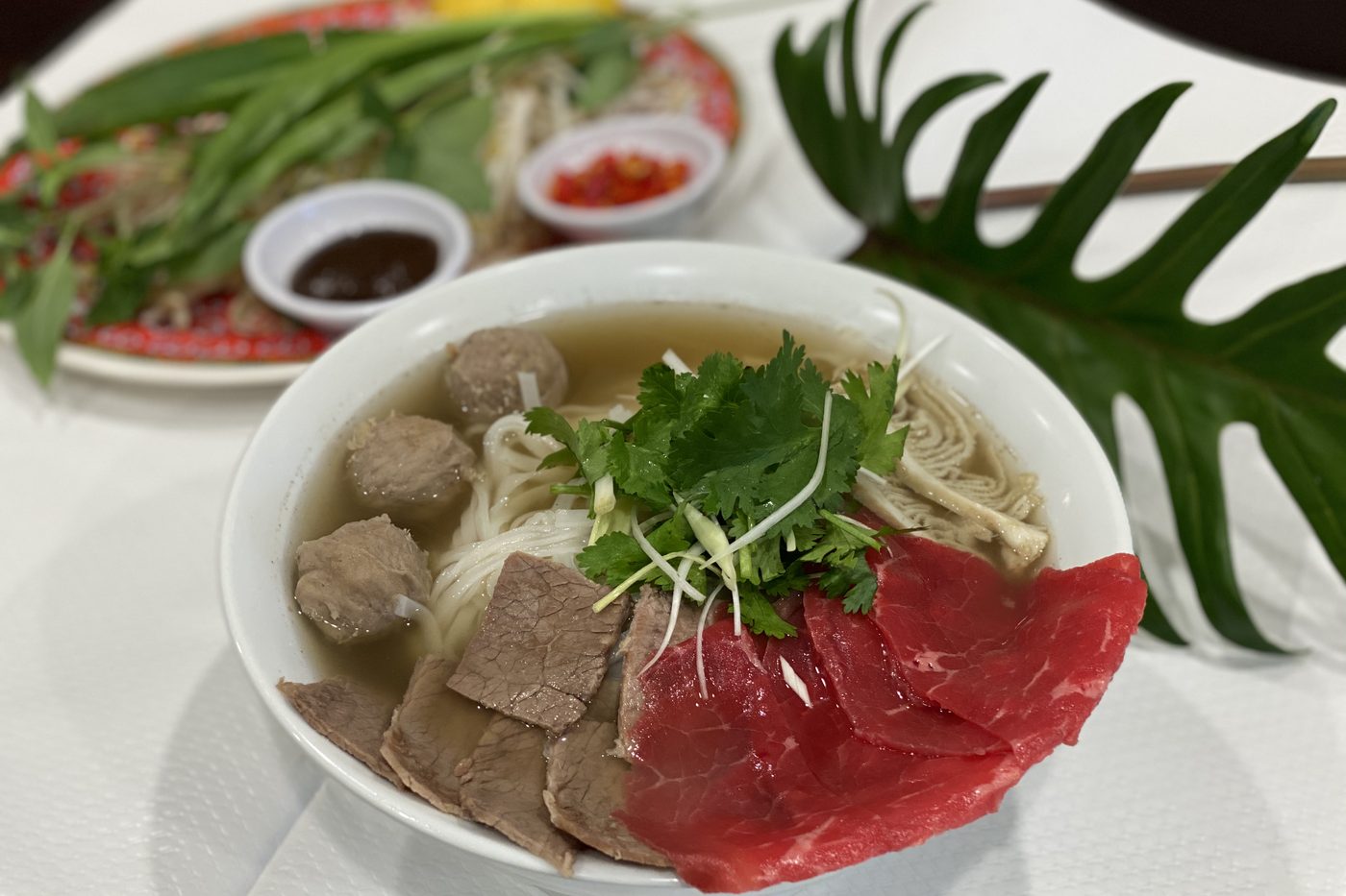 Un bol de pho dac biet, nouilles de riz, bœuf cru et cuit, boulettes et coriandre, avec l'assiette d'herbes