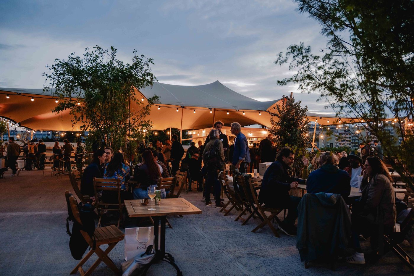 La terrasse de Plantation à la tombée du jour, tables en bois sous une grande tente, guirlandes lumineuses