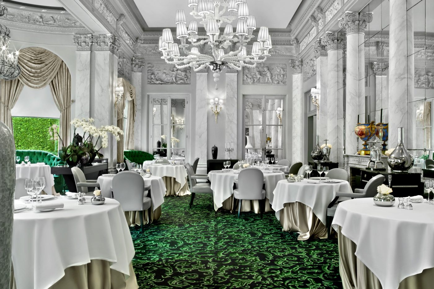 La grande salle du Pré Catelan, colonnes blanches, lustre de cristal, moquette verte et tables nappées de blanc