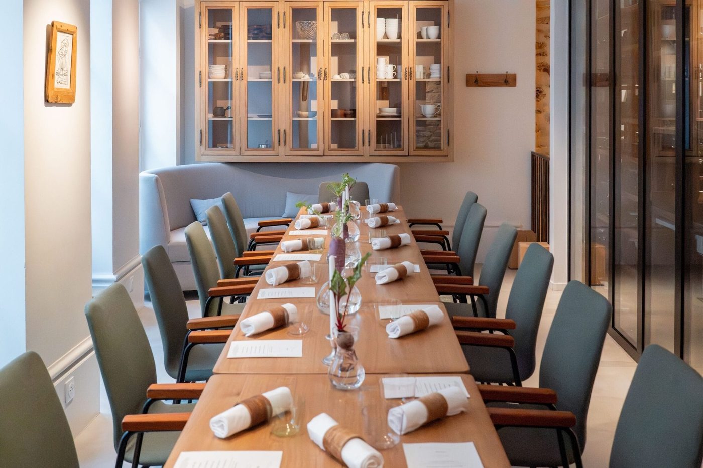 La salle de Prévelle dressée en longue table de bois clair, chaises vert-de-gris et vaisselier vitré au fond