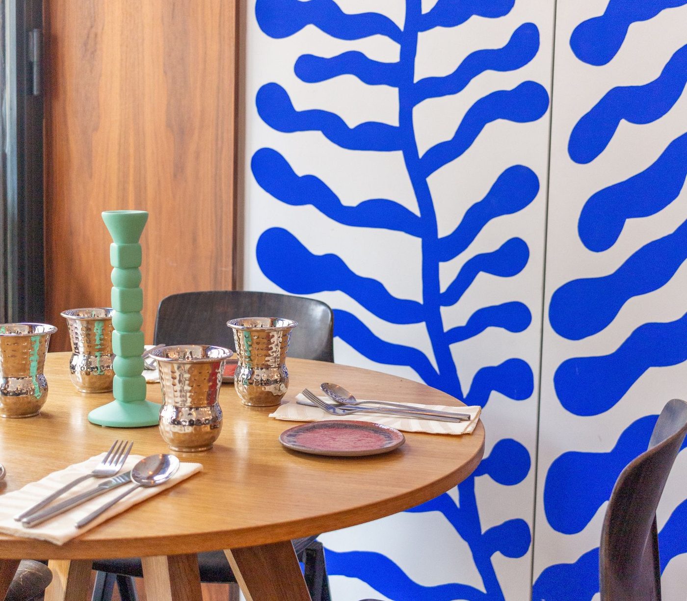 Une table ronde dressée devant les fresques de feuillages bleus de Qasti Bistrot