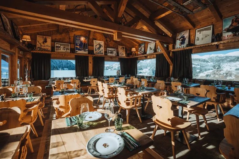 La salle boisée du Relais des Fermes, chaises sculptées, tables dressées et grandes fenêtres sur la montagne