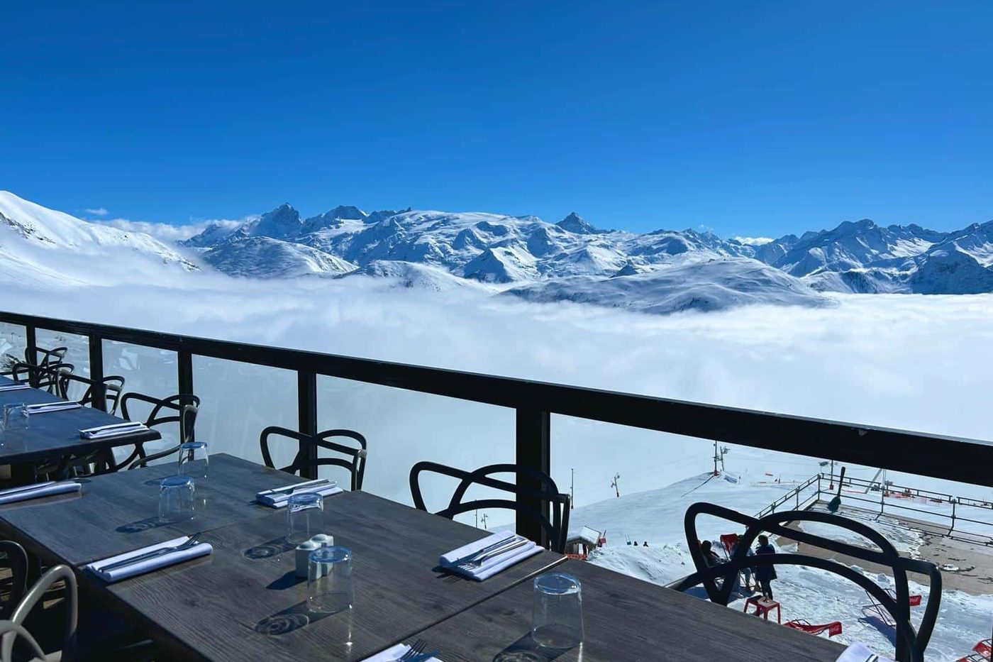 Tables dressées sur la terrasse vitrée de Signal 2108, au-dessus d'une mer de nuages, sommets enneigés au loin