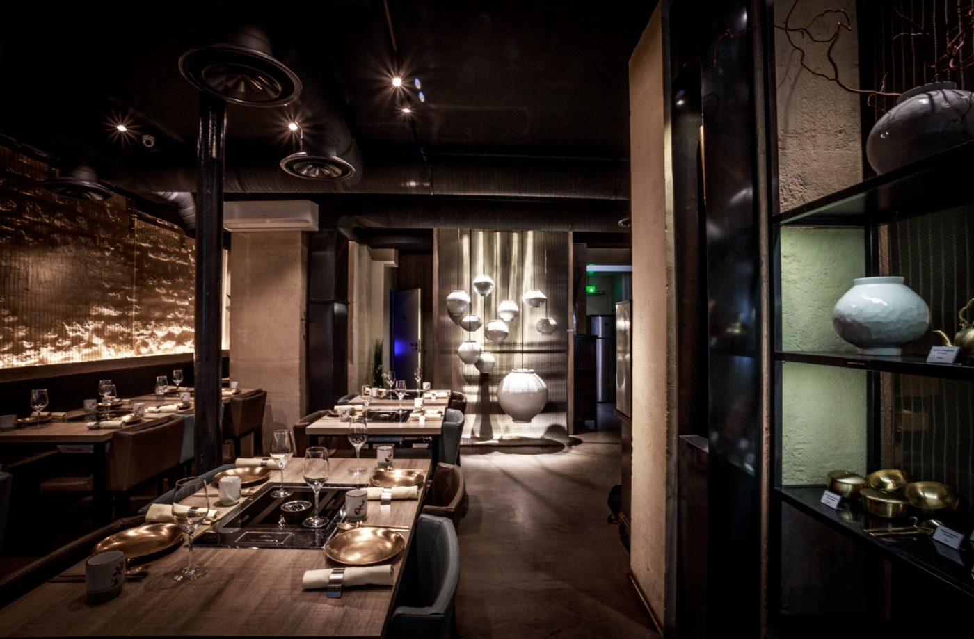 La salle de Soon Grill, tables en bois à grill encastré, hottes au plafond et jarres de porcelaine blanche