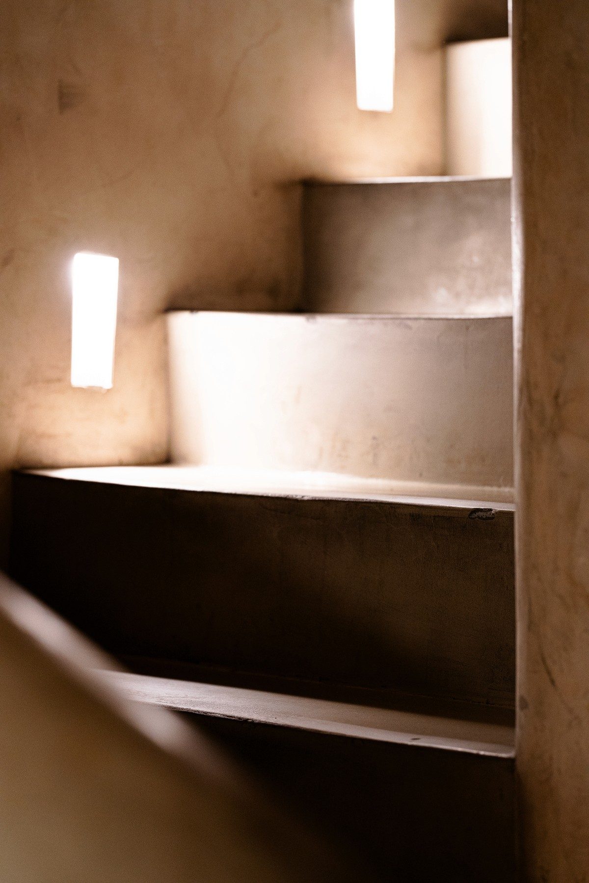 Un escalier aux murs enduits, éclairé par de fines ouvertures, à La Table de Mee