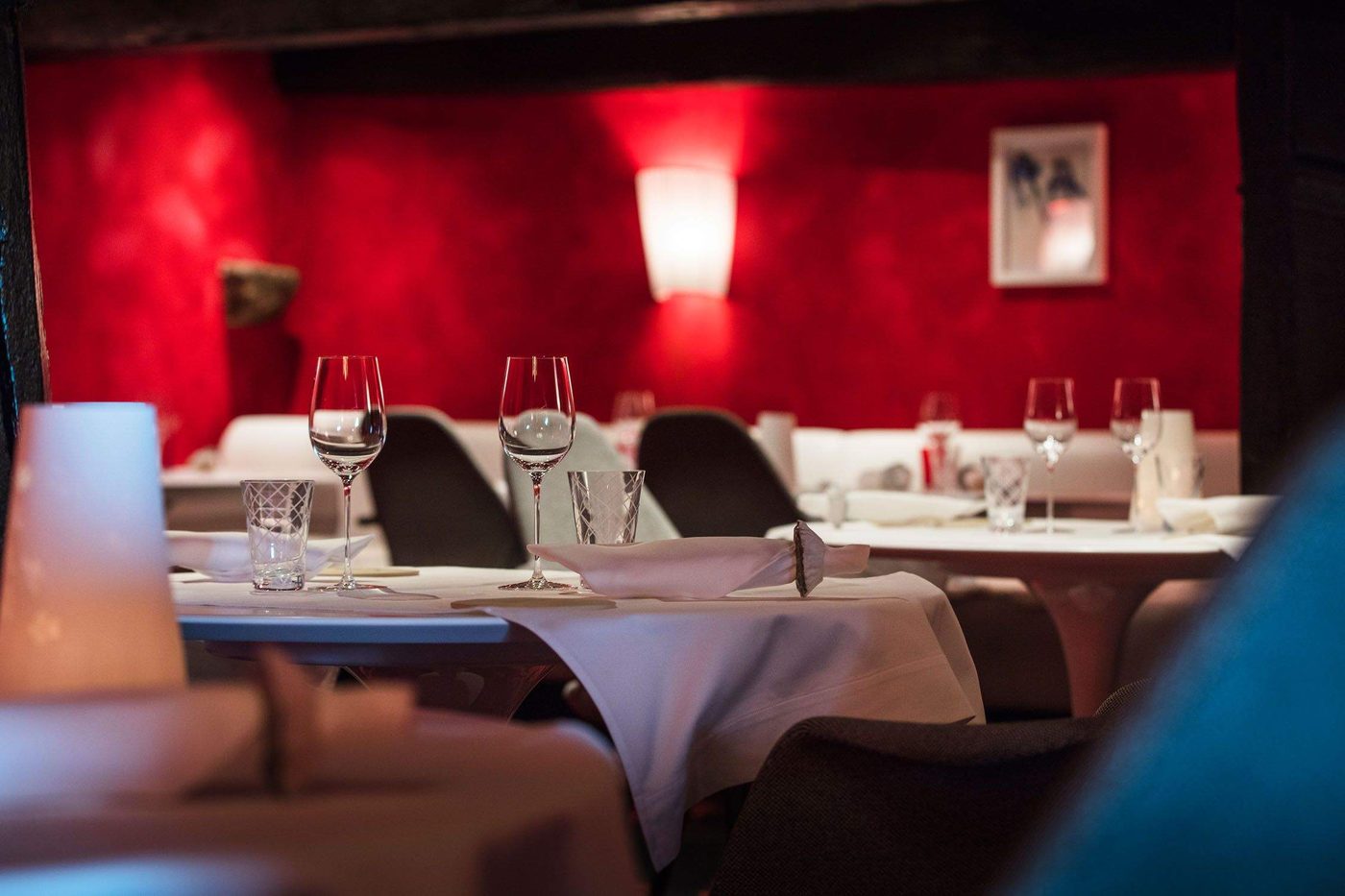 La salle de La Table du Gourmet : mur rouge, applique lumineuse et tables rondes nappées de blanc