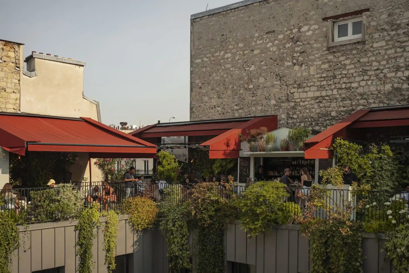 Le rooftop The Shed en fin de journée, auvents rouges, bar en cabane et tables le long du garde-corps fleuri
