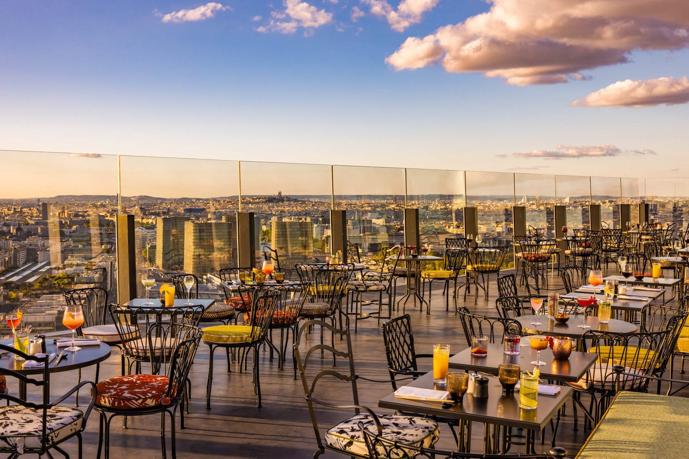 La terrasse du TOO TacTac, tables et chaises en fer forgé derrière un garde-corps vitré, Paris en contrebas