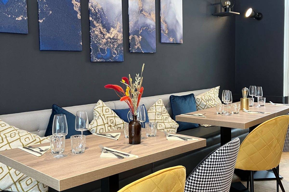 La salle du Tova, banquette garnie de coussins, tables de bois clair, chaises jaunes et tableaux bleus au mur