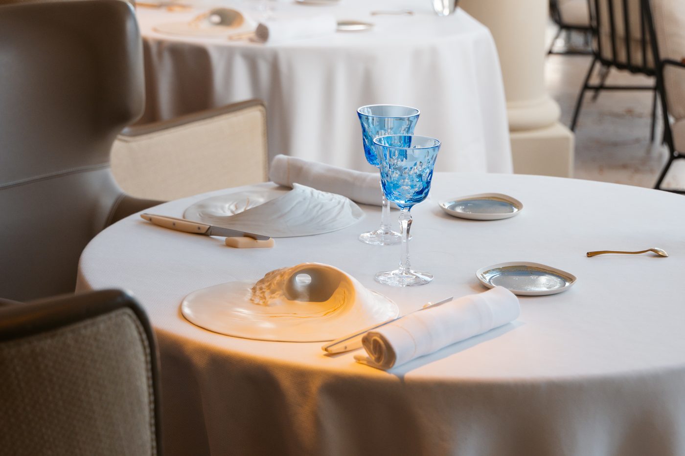 Une table dressée à La Vague d'Or, nappe blanche, verres bleus et assiette en forme de coquillage