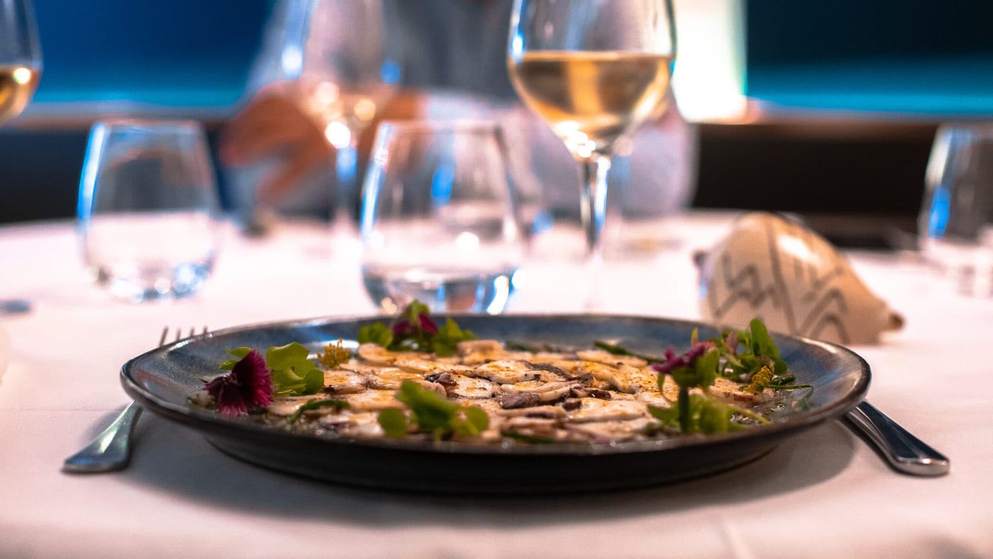 Une assiette de poisson du Vent d'Armor dressée sur nappe blanche, verres de vin blanc en arrière-plan