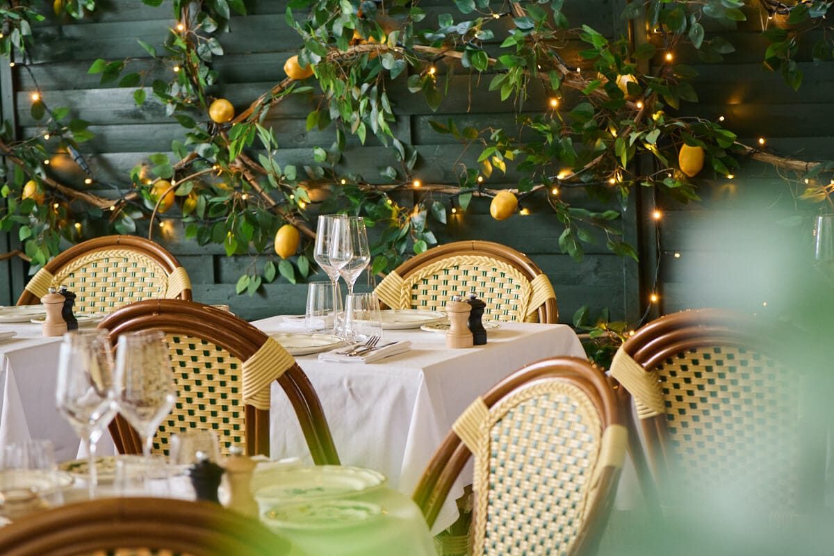 Le patio de Zeffirino Paris, tables nappées de blanc et chaises cannées devant un mur végétal garni de citrons